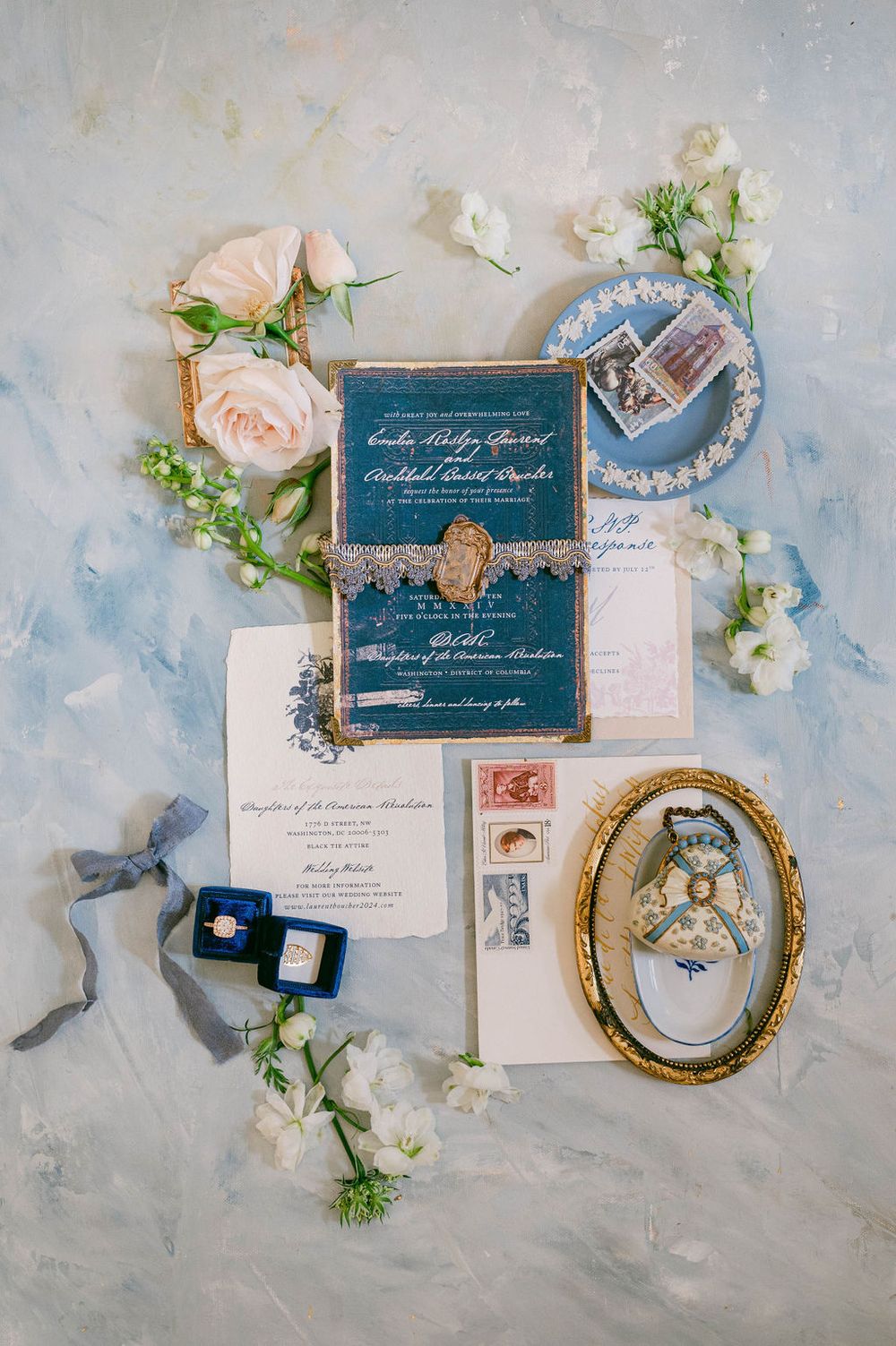 Elegant navy and gold wedding invitation suite with floral accents and vintage frames laid on light marble surface.