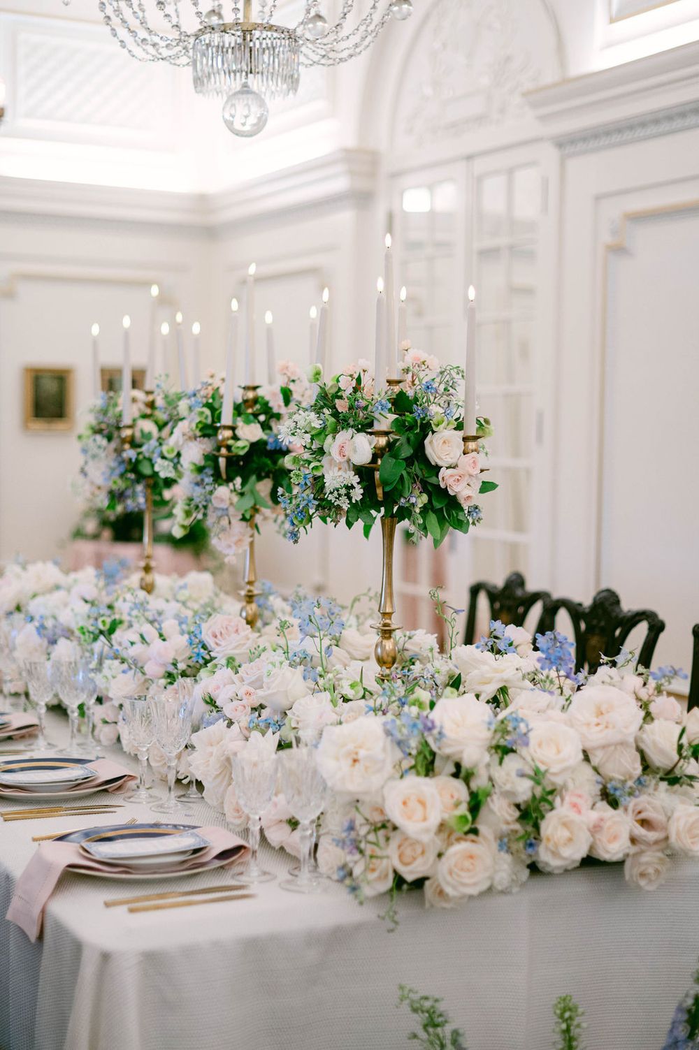 Elegant wedding reception tables decorated with blue and white floral arrangements and crystal chandeliers.