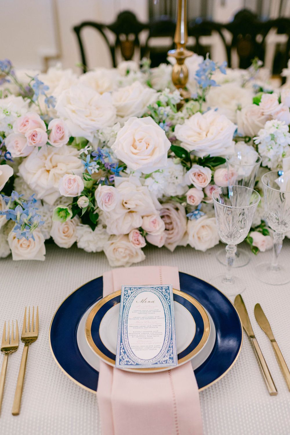 Elegant wedding table setting with pink and white roses, navy charger plates, and gold cutlery in a modern reception.