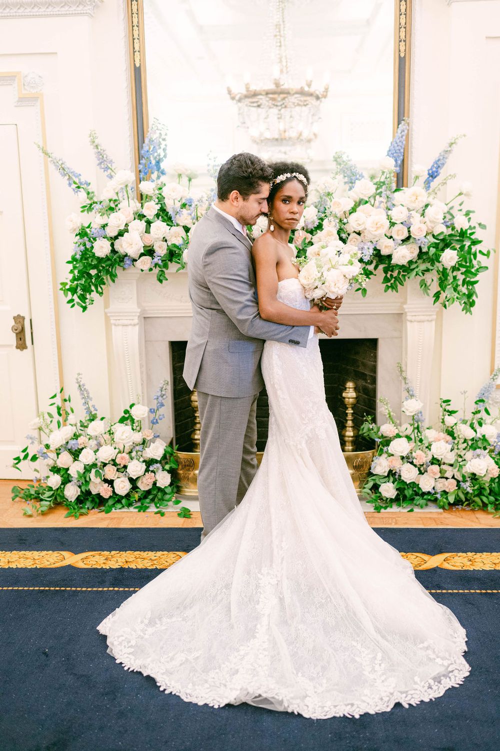 Romantic wedding couple dancing together in an elegant ballroom decorated with white floral arrangements and greenery.