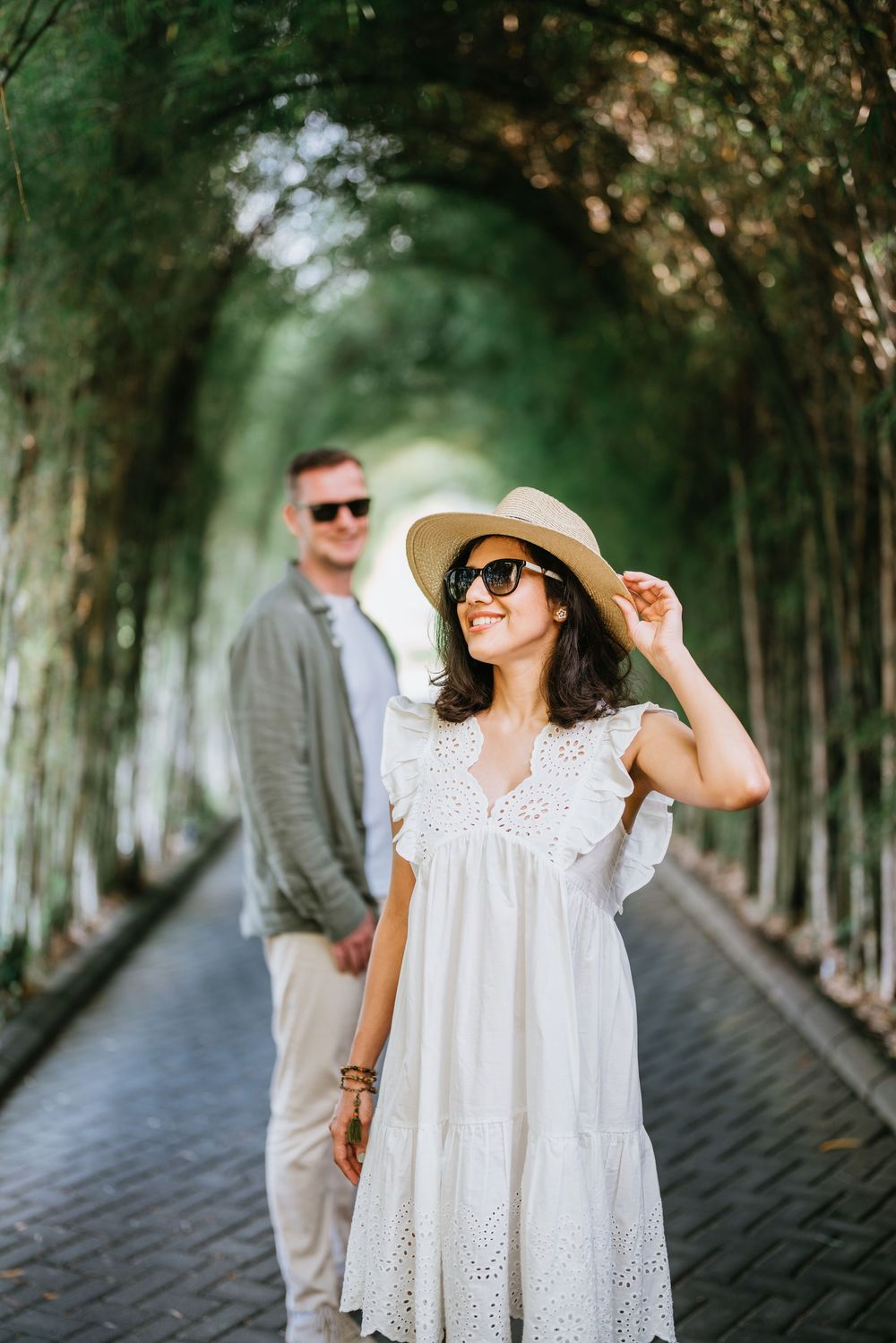 A couple poses in a tree-lined pathway with sunlight filtering through the branches.