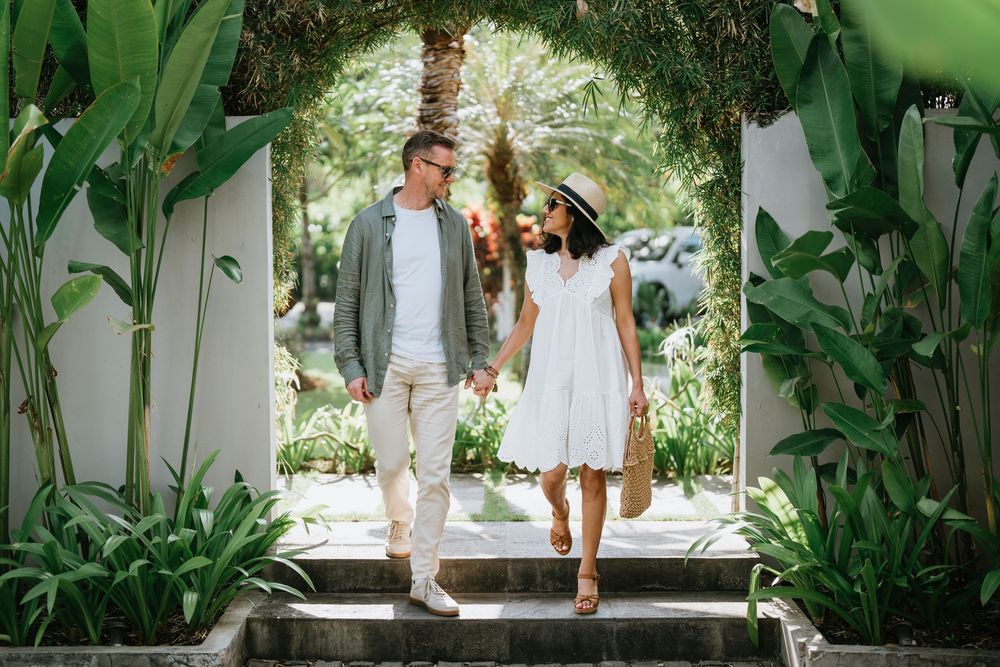 A couple walks through a tropical garden archway with lush greenery.