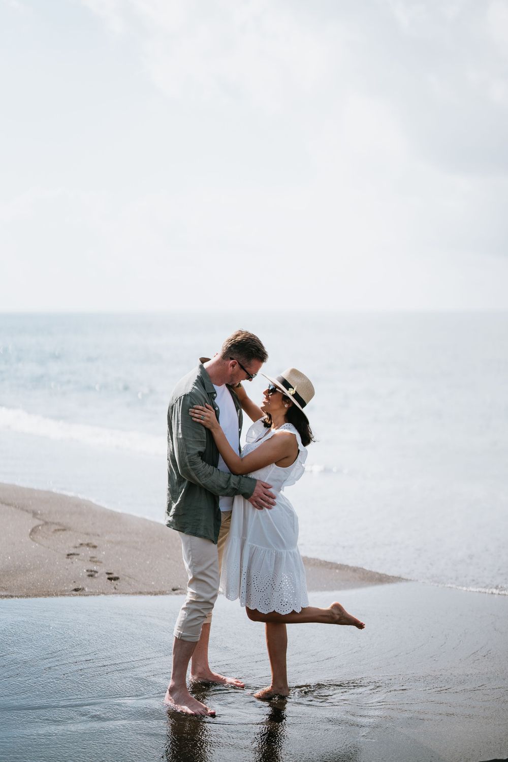 A romantic moment captured on a beach as waves lap at their feet during sunset.