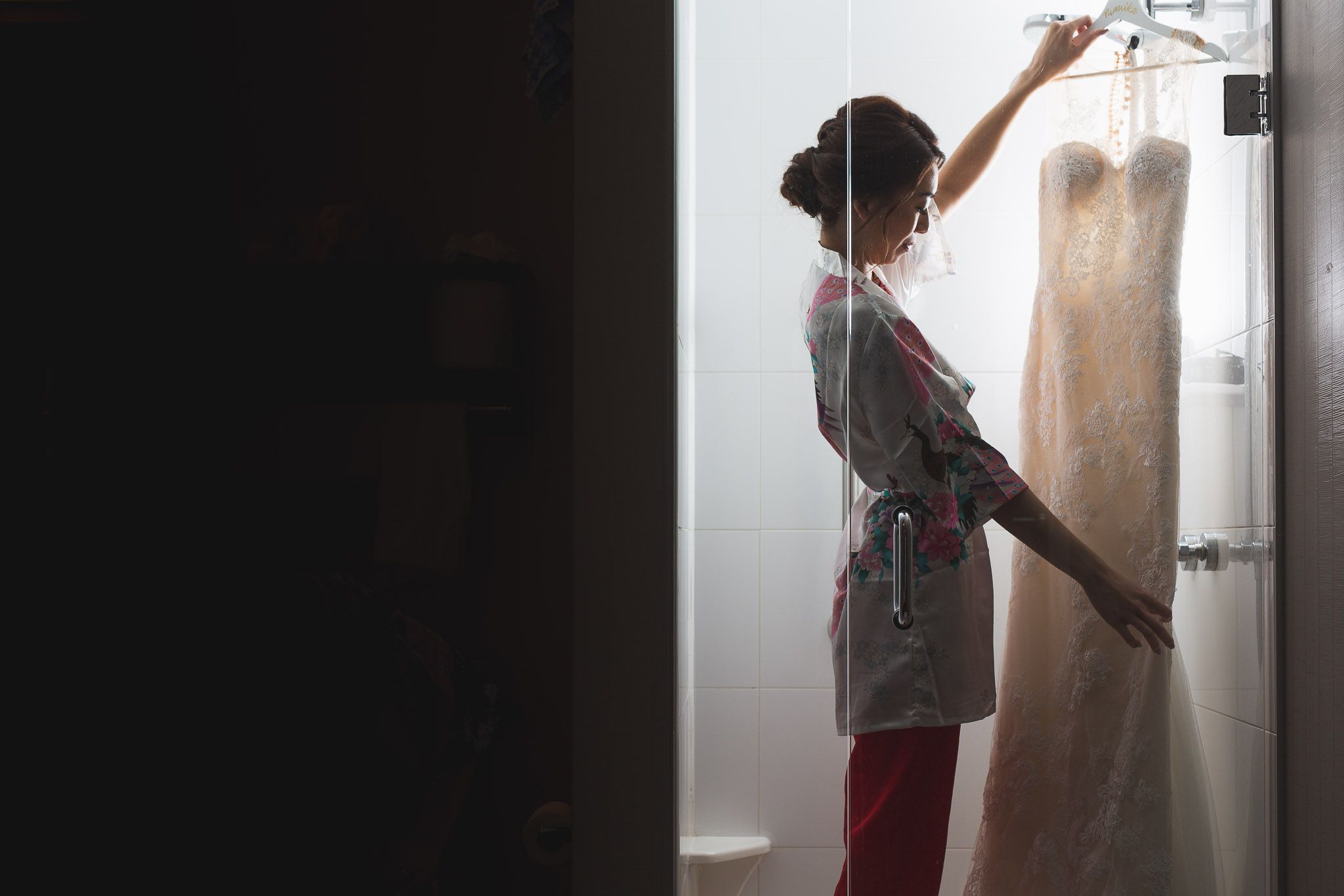 Silhouette of someone reaching up to adjust a wedding dress hanging in a doorway.