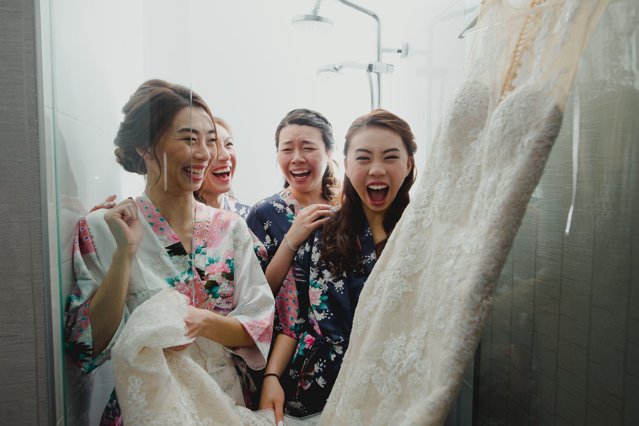 Wedding party members share joyful moments while preparing in a bright room with white dresses.