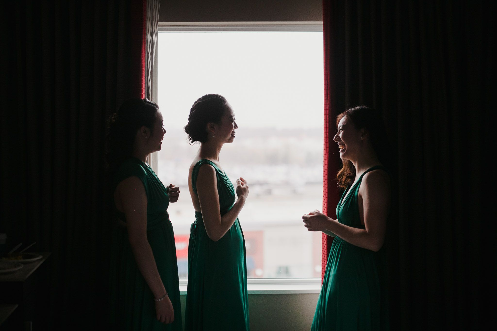 Silhouetted figures in formal attire stand against bright windows during an intimate wedding ceremony.