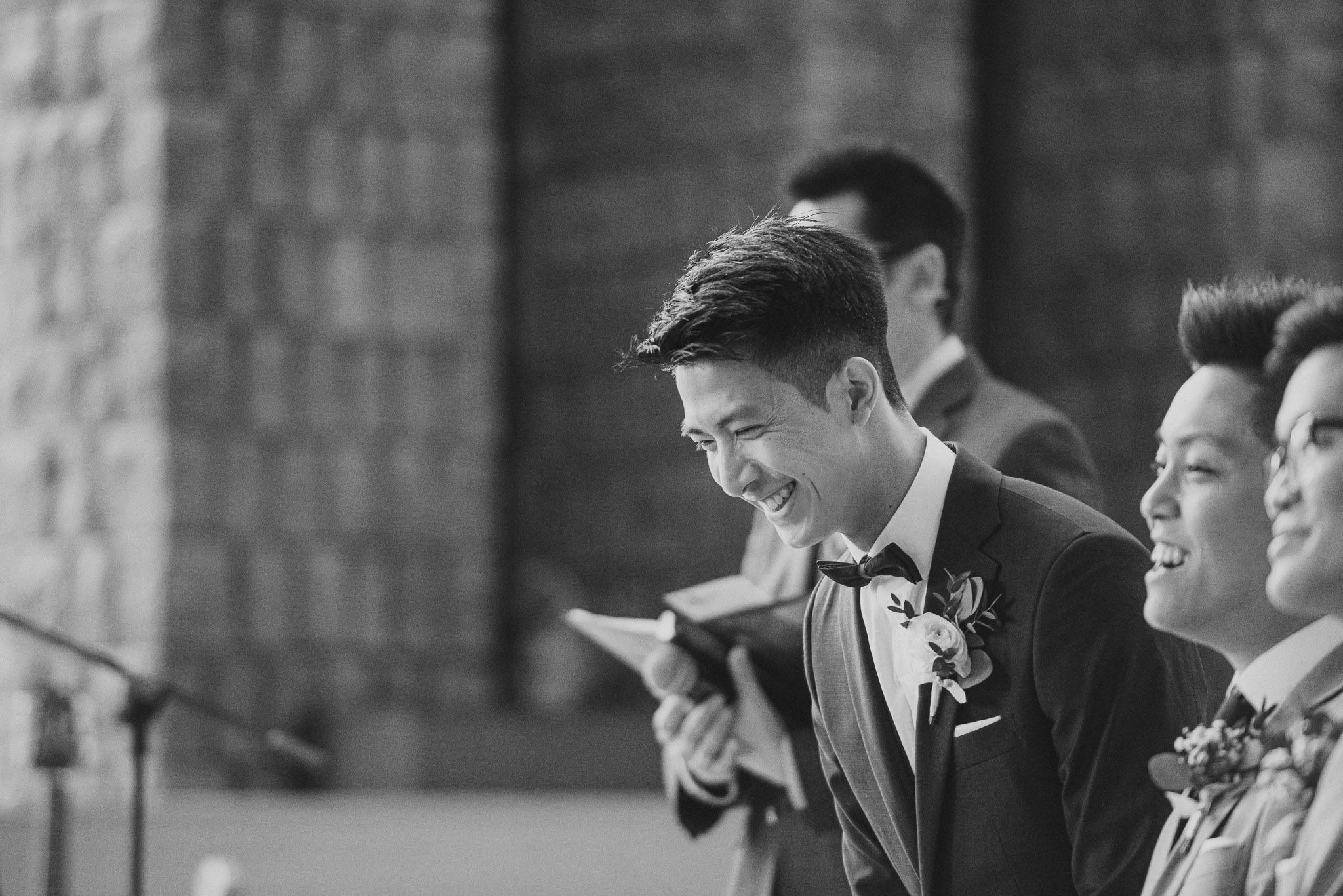 Groomsmen share a joyful moment during a wedding ceremony, captured in black and white photography.