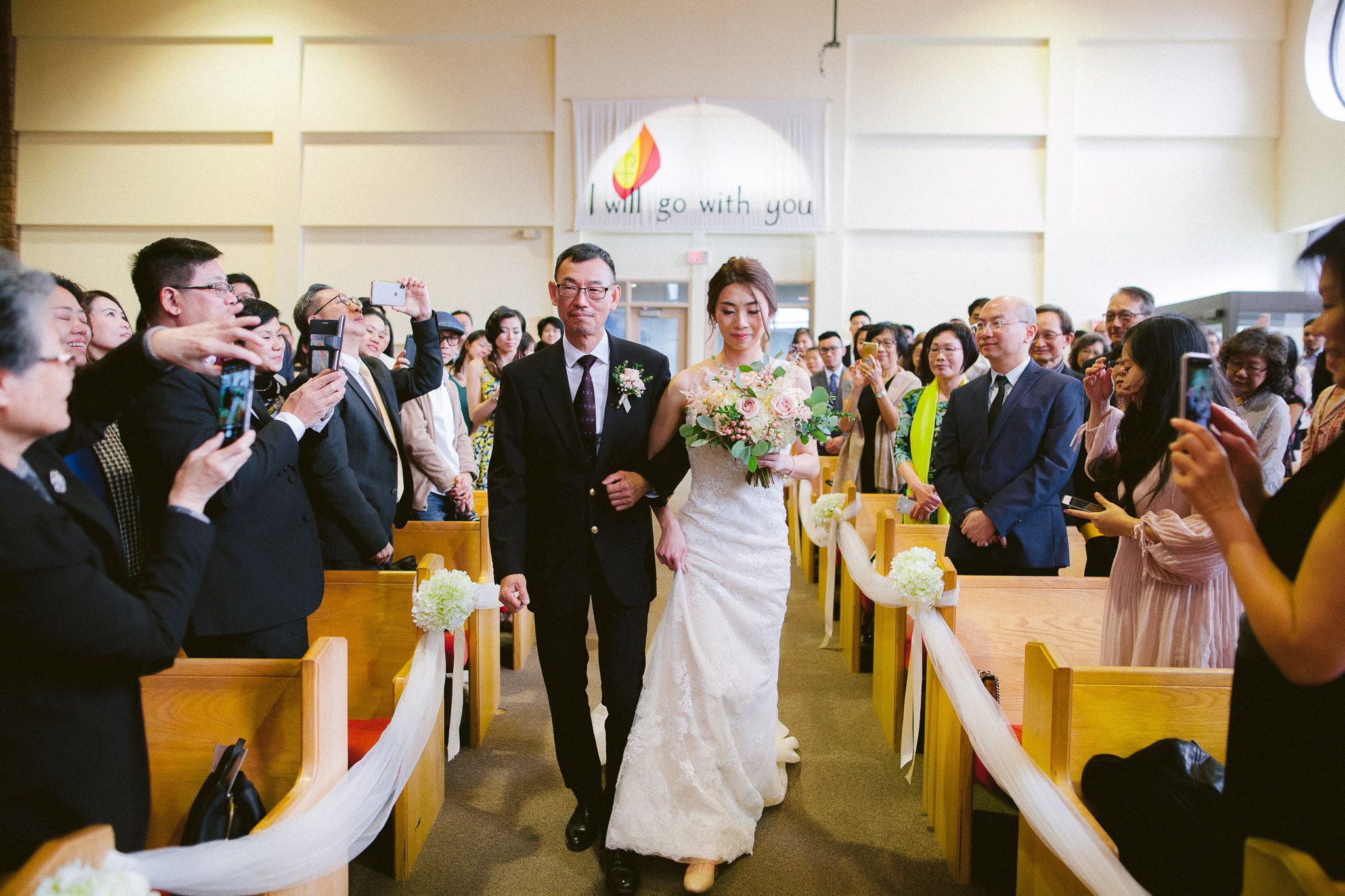 Wedding ceremony in a bright church hall with guests seated in rows watching the celebration.
