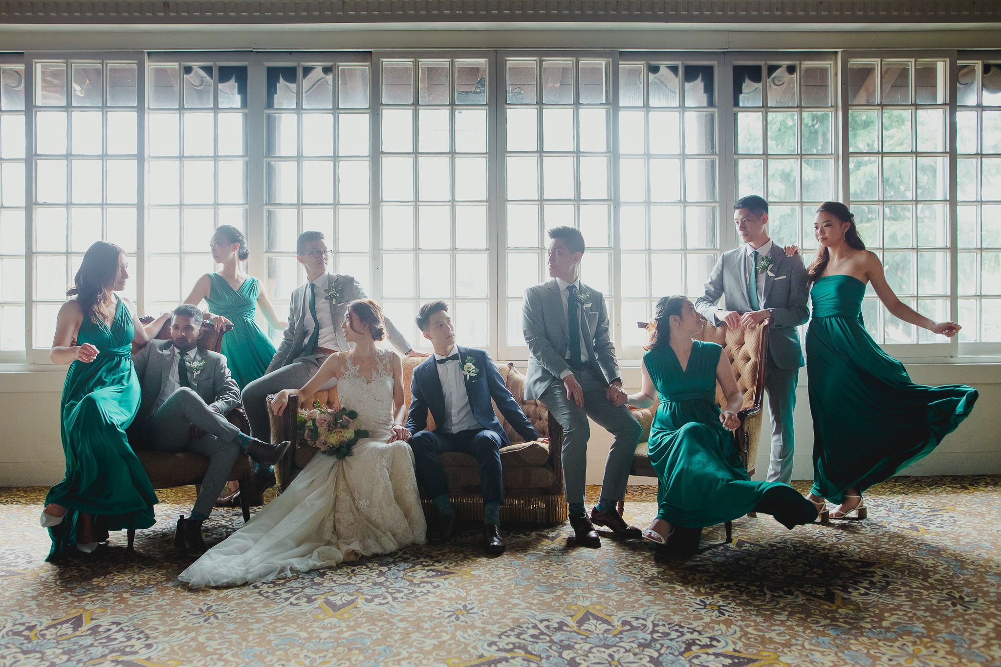 Wedding party group photo with large windows and natural lighting.