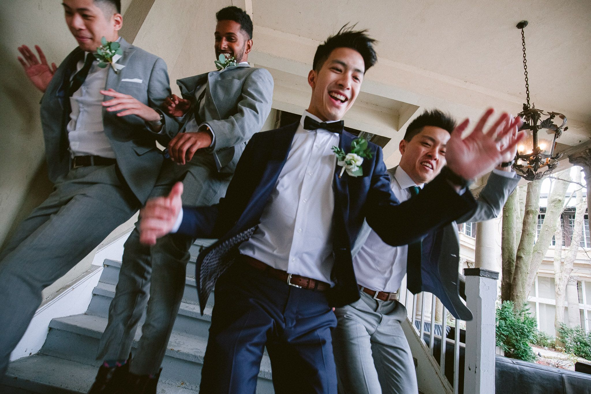 Groomsmen in gray suits jumping and posing playfully for a wedding photo.