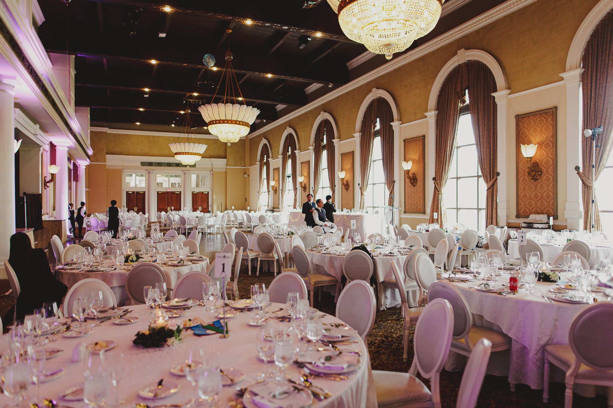 Elegant wedding reception hall with arched columns and tables set with pink linens and white chairs.