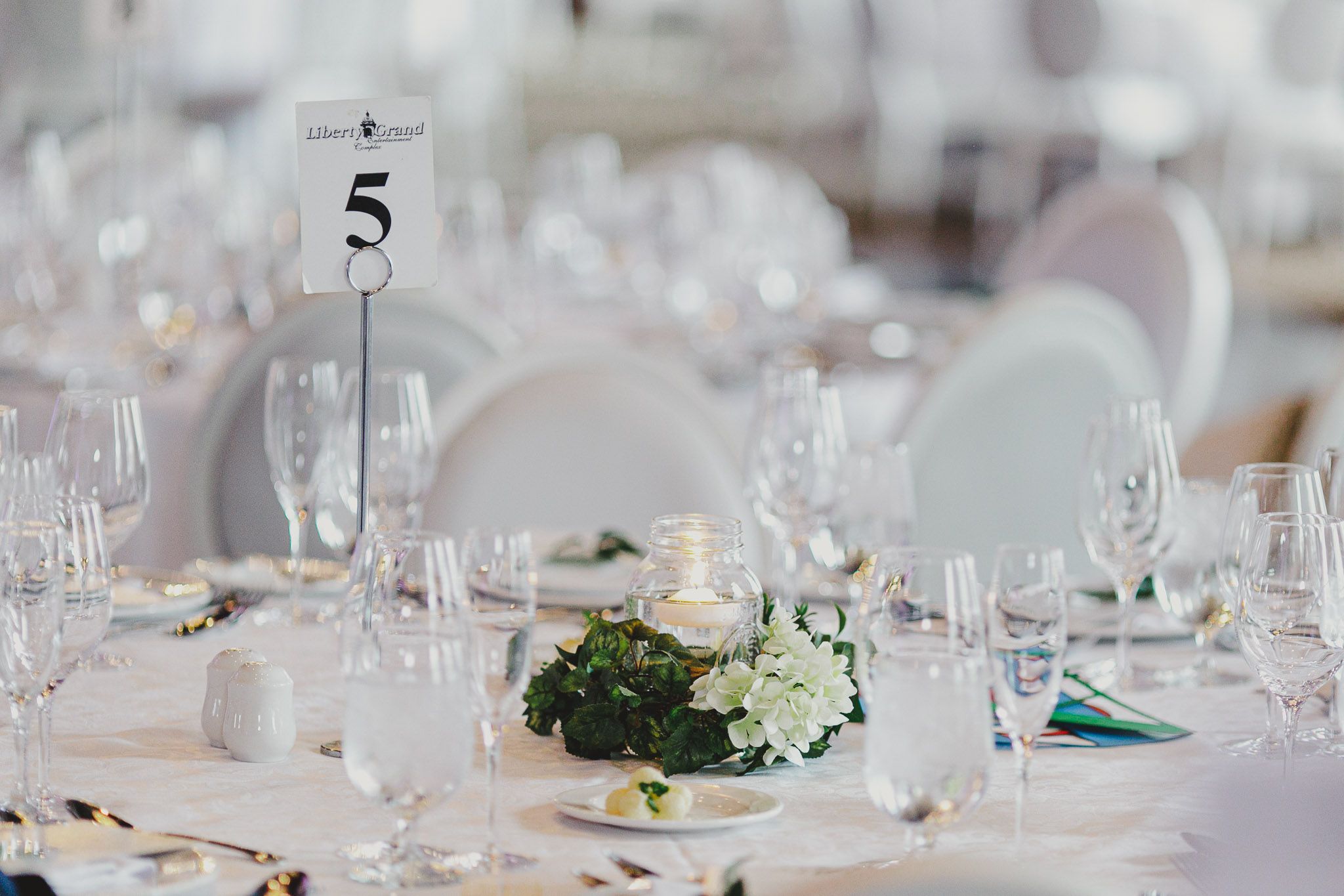 Elegant wedding reception table settings with white floral centerpieces and crystal glassware.