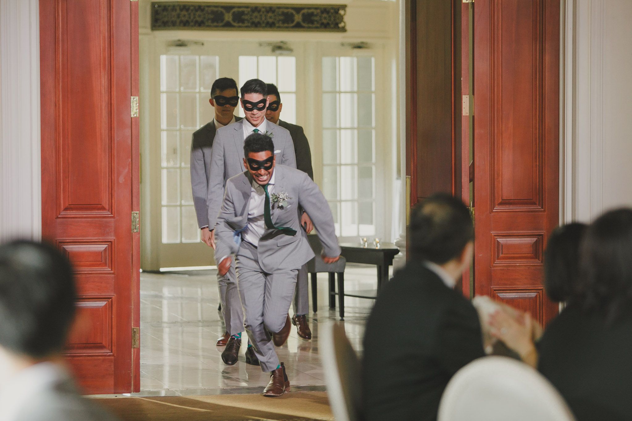 Wedding party members in formal attire running and leaping through red doorways.