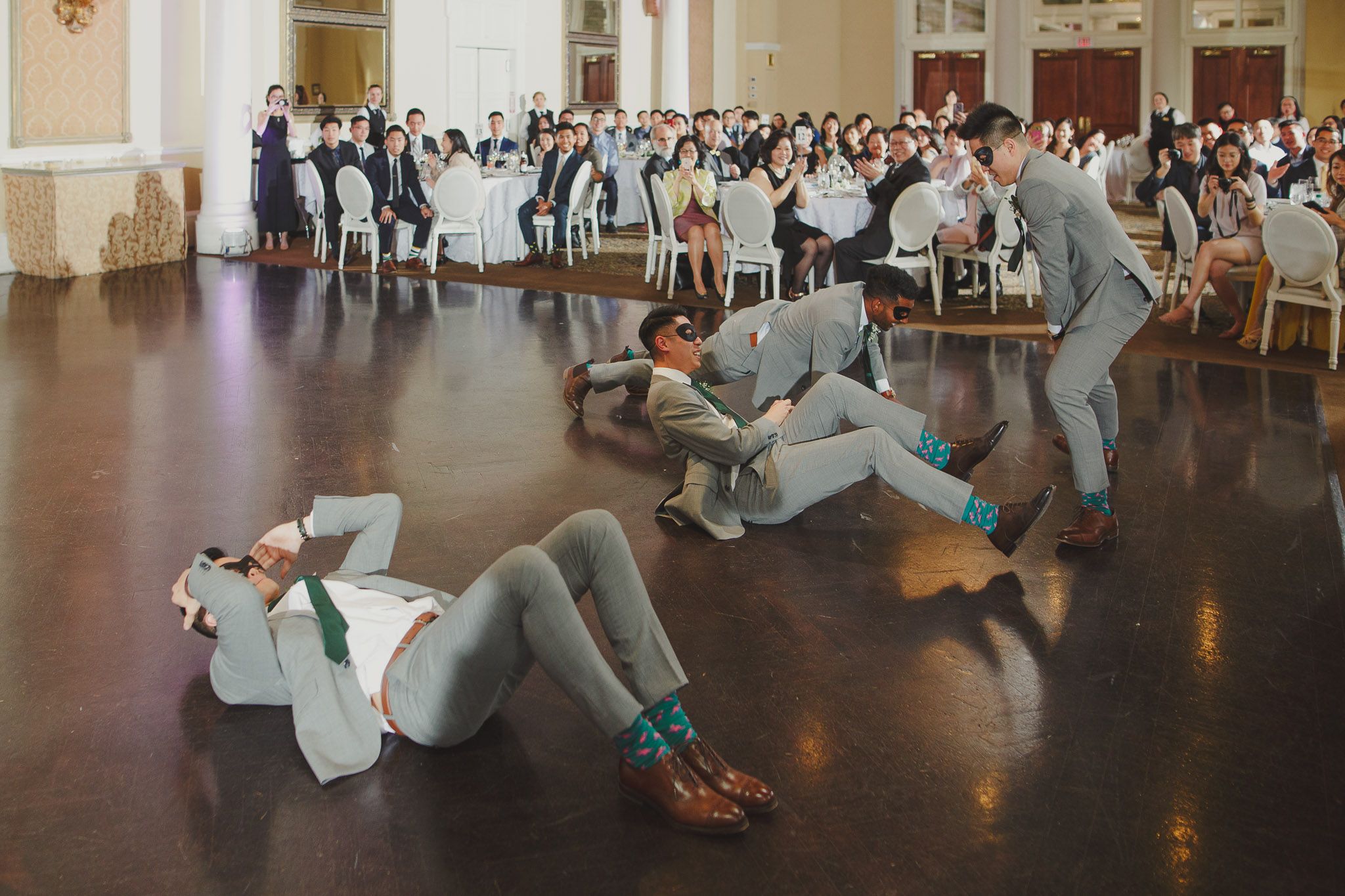 Wedding guests performing synchronized dance moves on a wooden dance floor during a reception celebration.