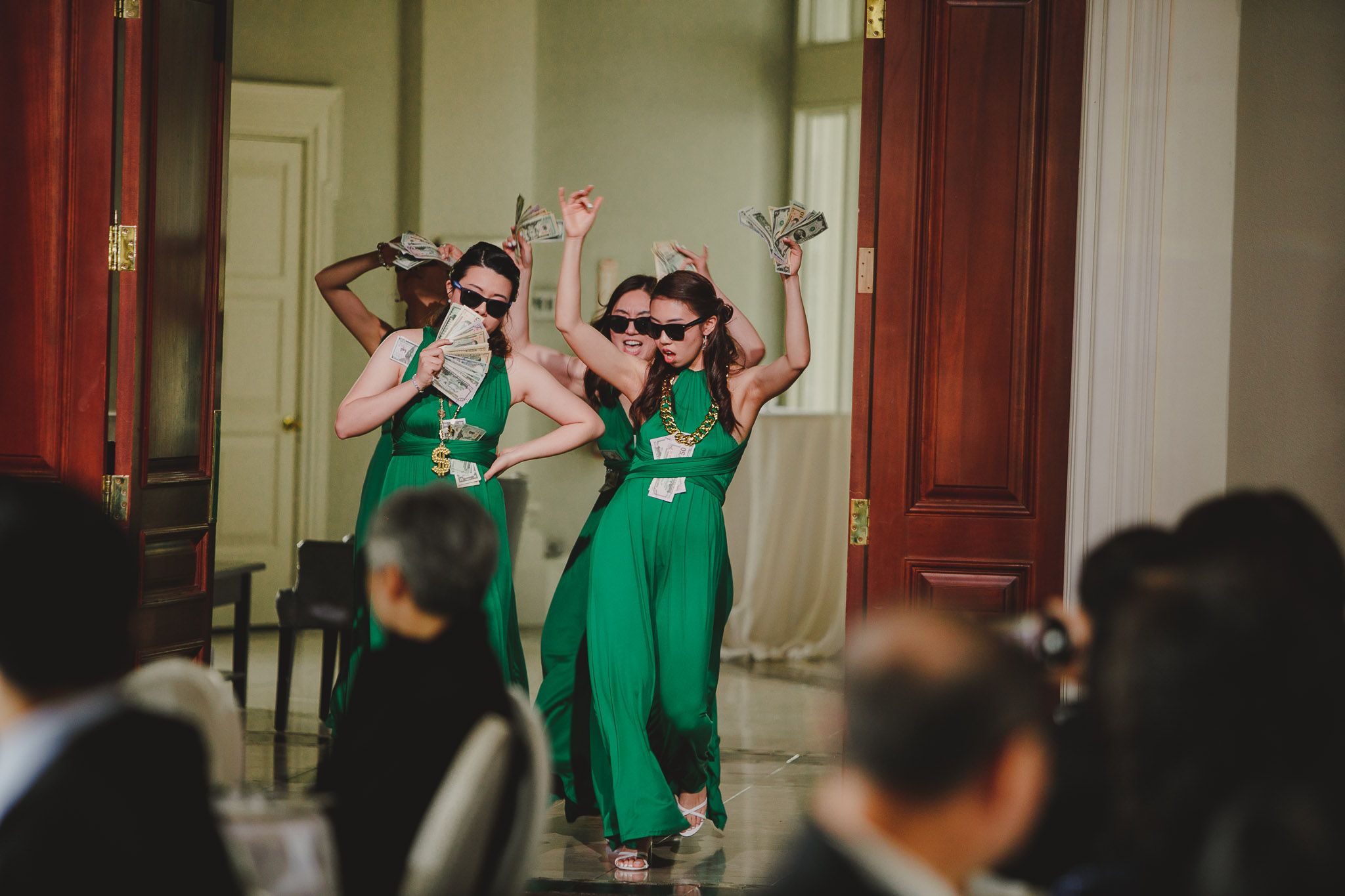 Bridesmaids in matching green jumpsuits dance energetically at wedding reception.
