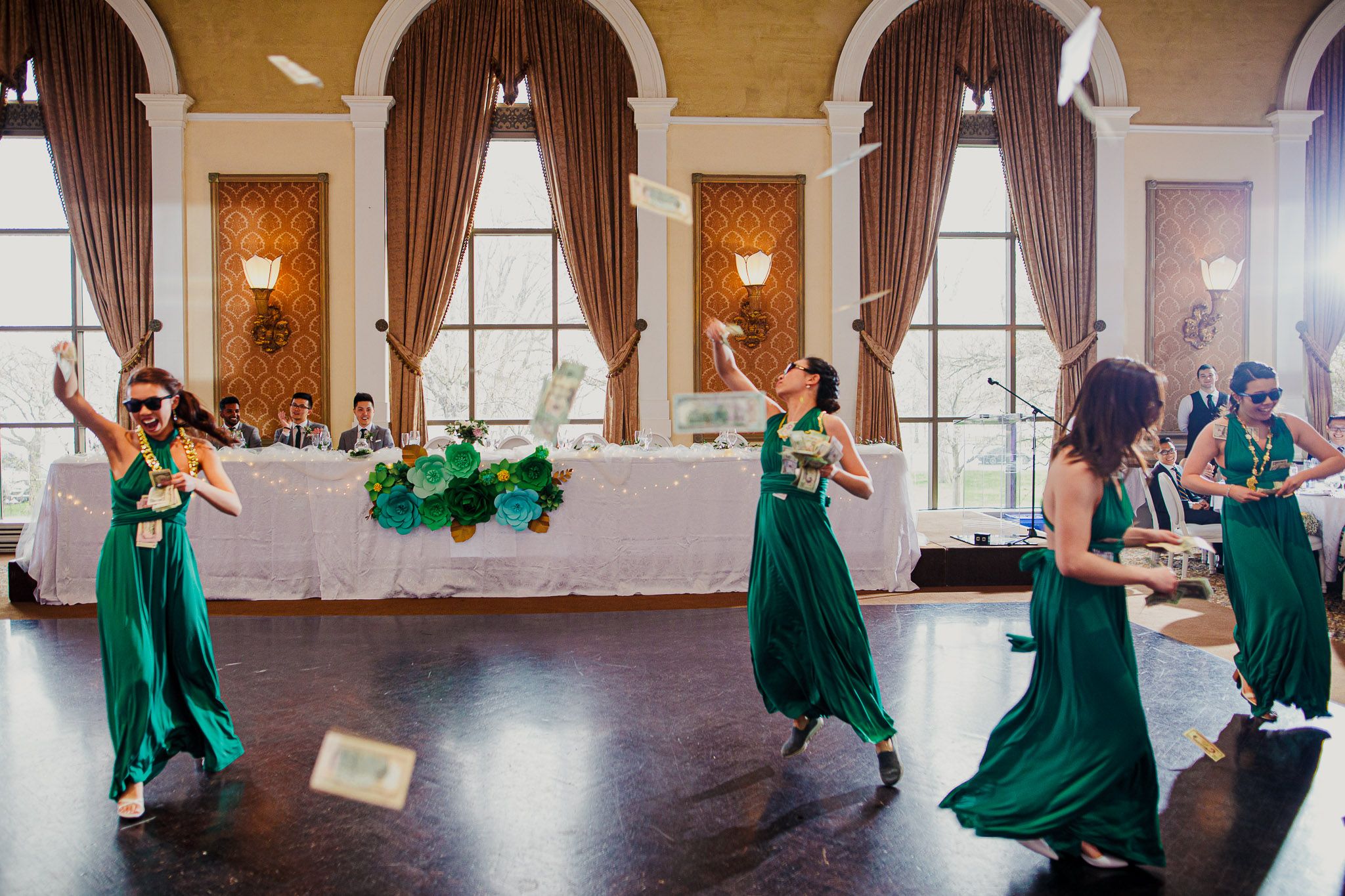 Wedding reception scene with bridesmaids in emerald green dresses dancing in an elegant ballroom.
