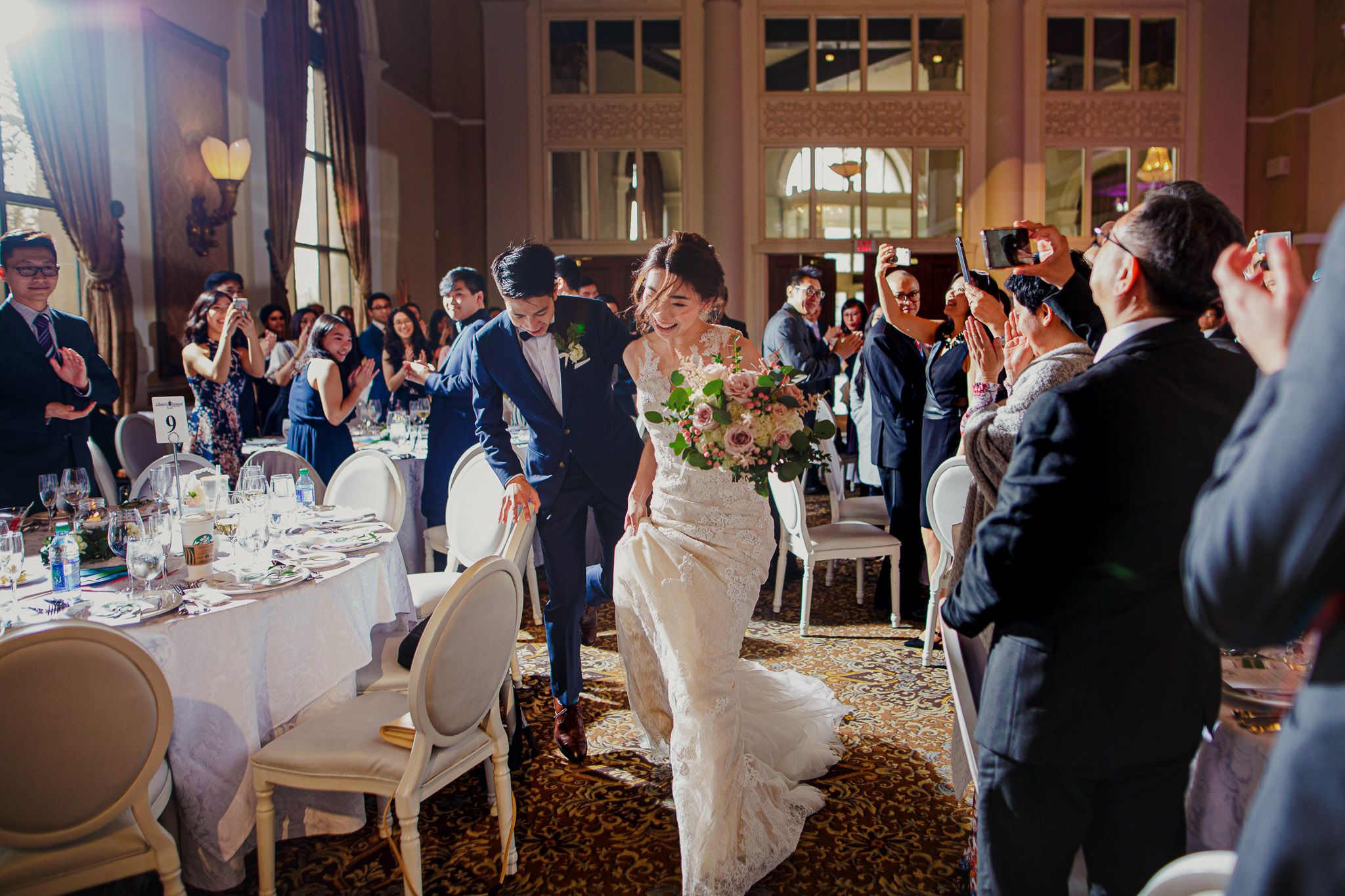 A wedding reception scene in an elegant ballroom with guests applauding the newlyweds.