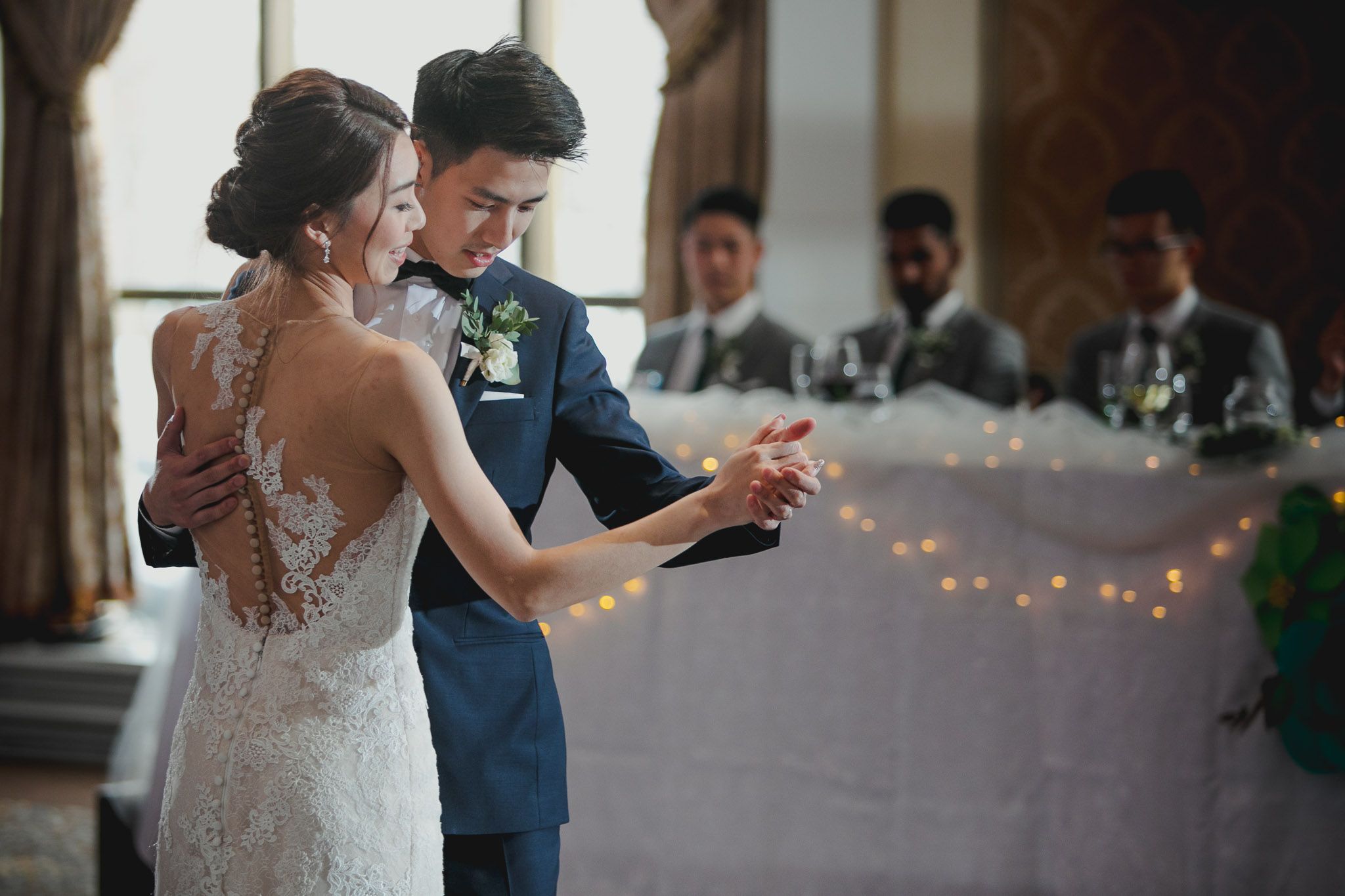 Couples dancing together at an elegant indoor wedding reception with string lights and decorative details.