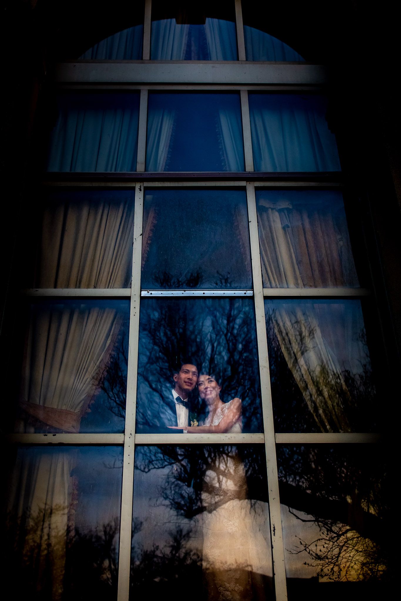 Silhouette of a dancing couple seen through arched windows at dusk with trees in the background.