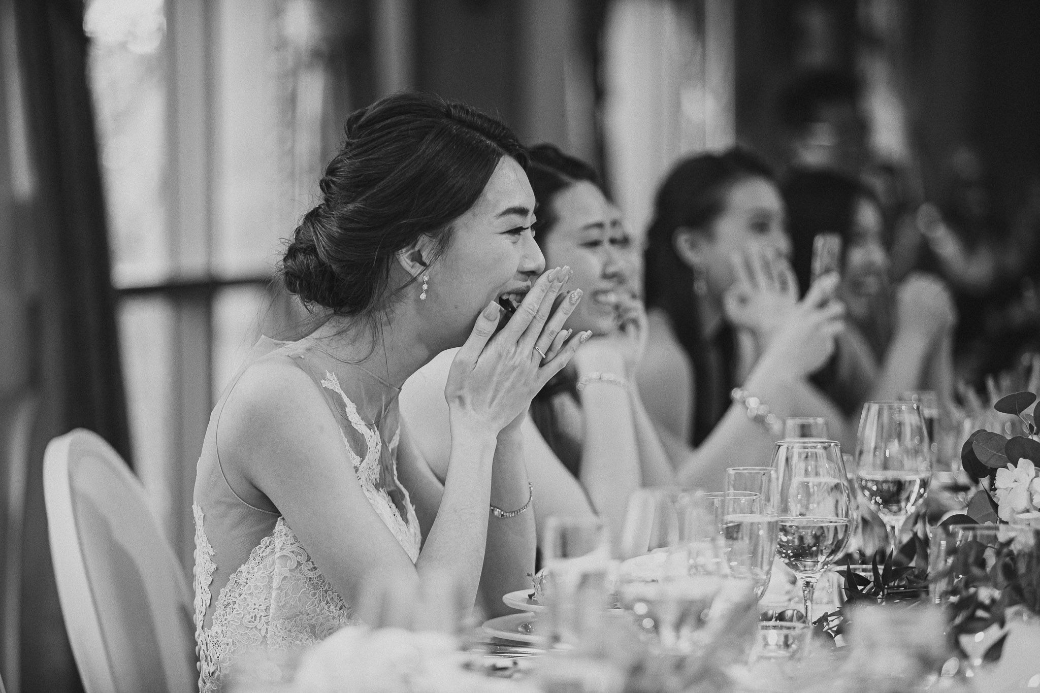 Wedding guests react with joy and laughter during an emotional reception moment at an elegant dinner table.