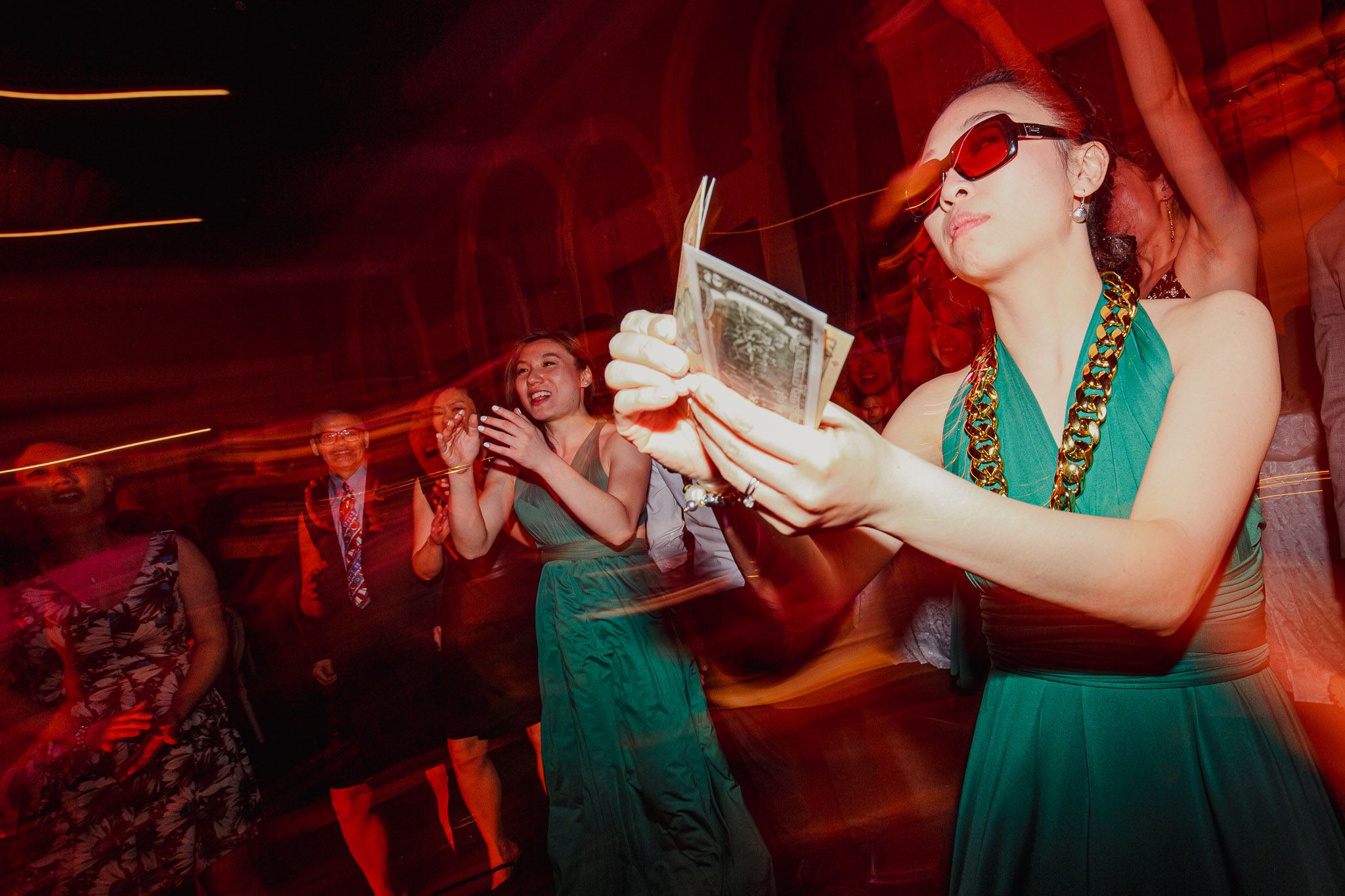 Party guests in matching green dresses dance and sing during a lively celebration.