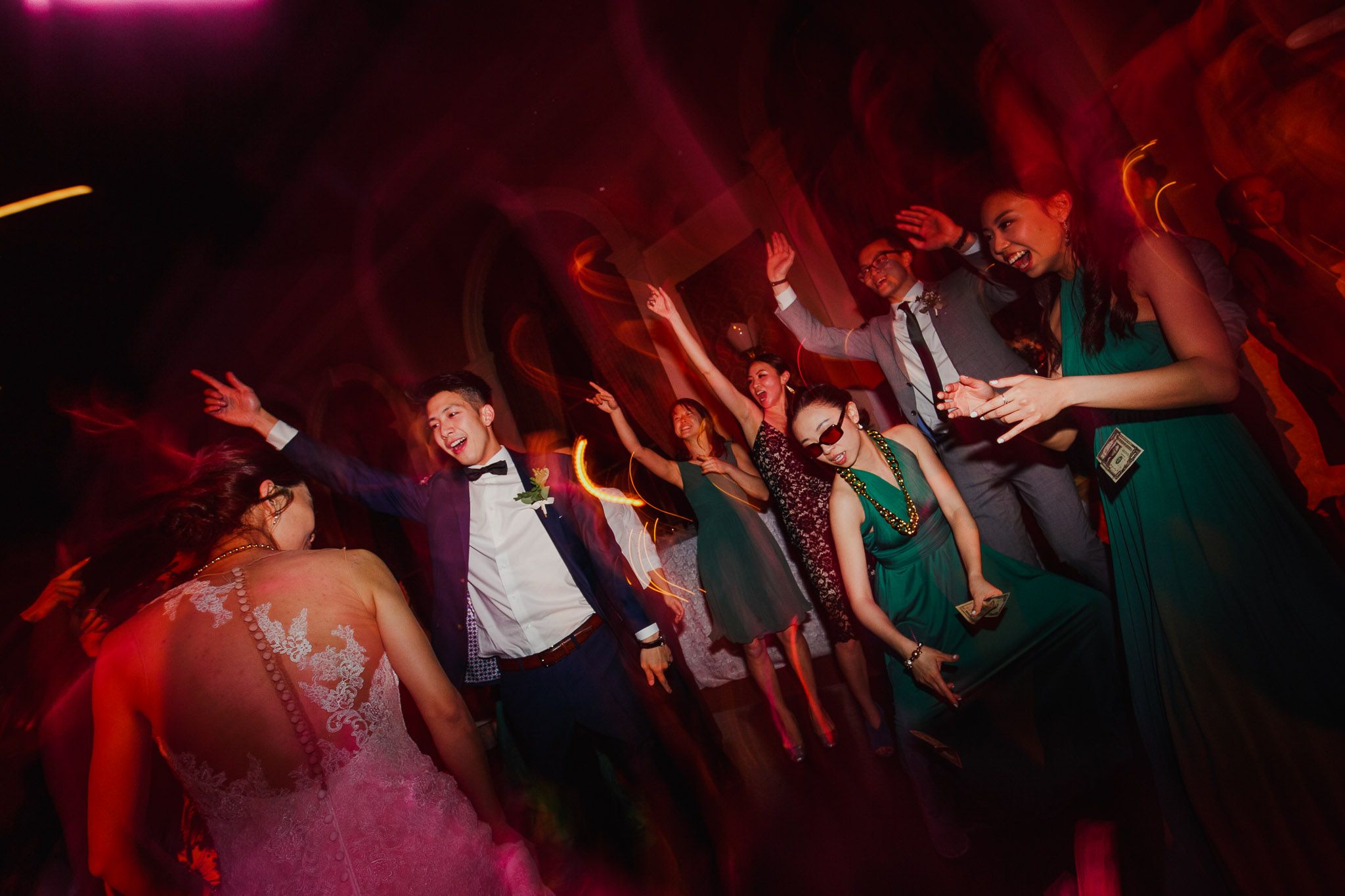 Dance floor filled with guests celebrating at a wedding reception with red and purple lighting.