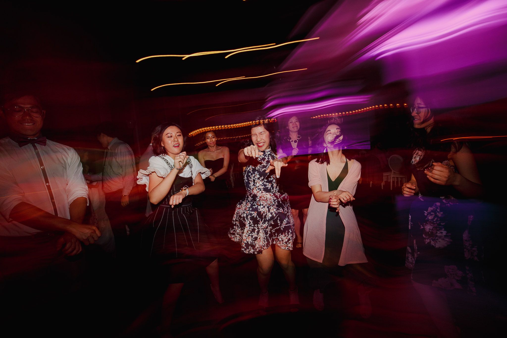 Party guests dancing under vibrant magenta lighting at a wedding reception.