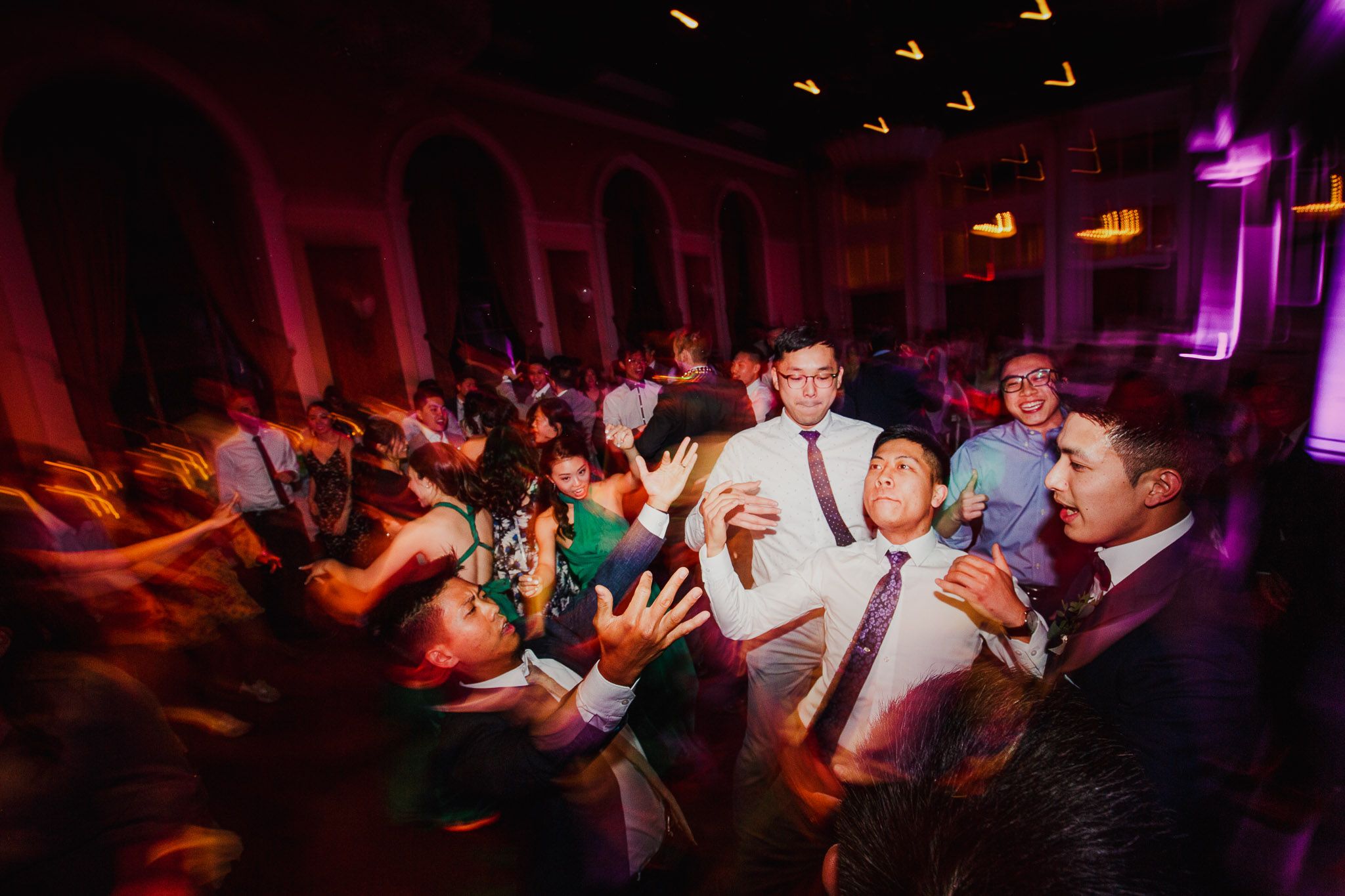 Crowded dance floor at wedding reception with purple ambient lighting.