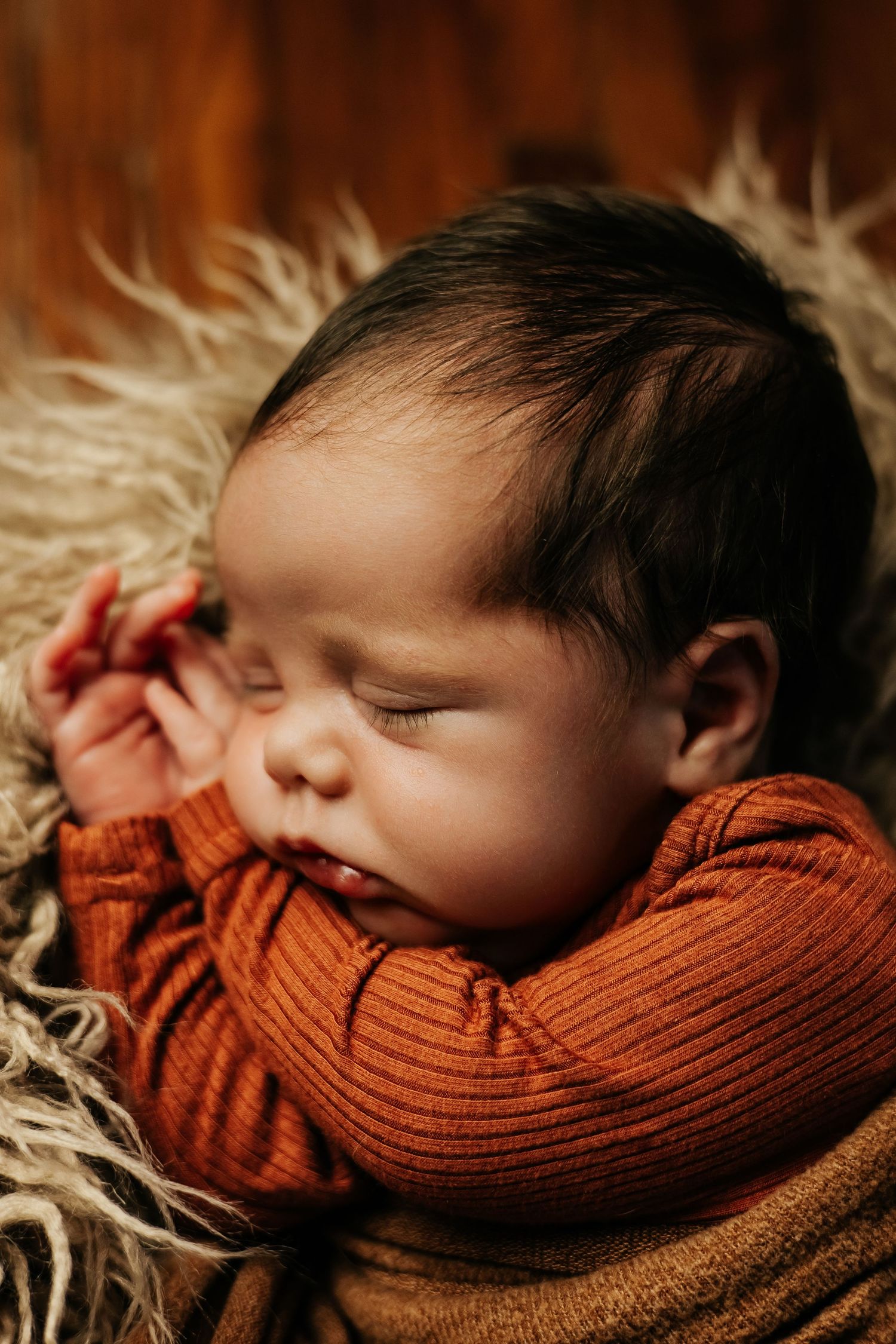 Newborn baby wearing orange wrap sleeping peacefully on textured backdrop.