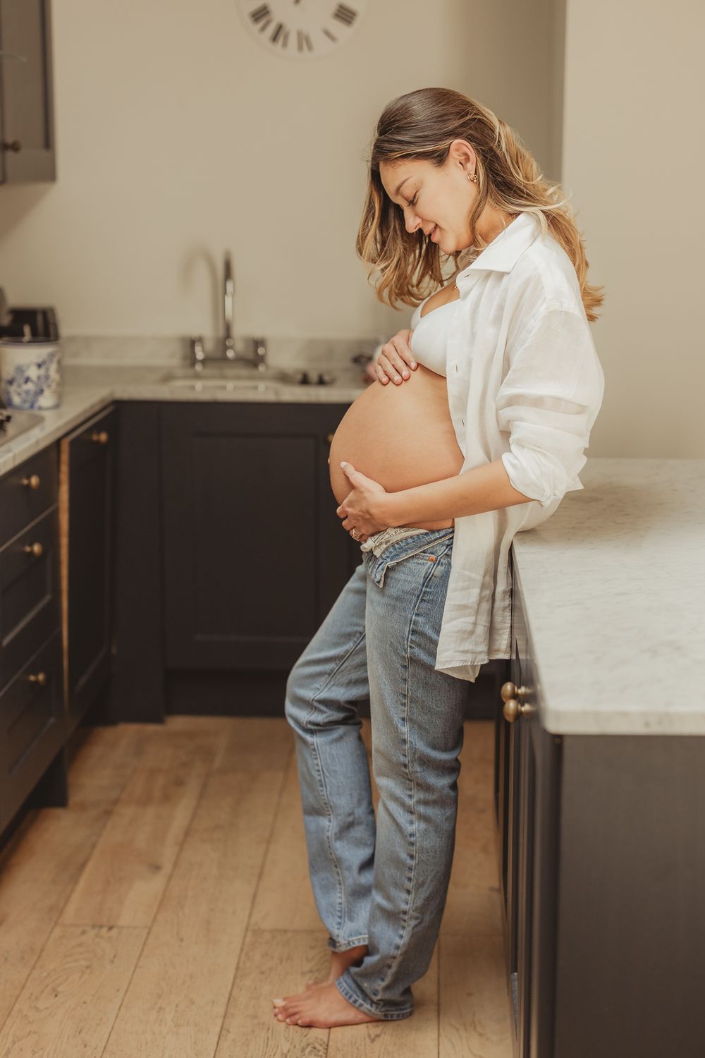 Natural maternity photos taken in a modern kitchen with wooden floors.