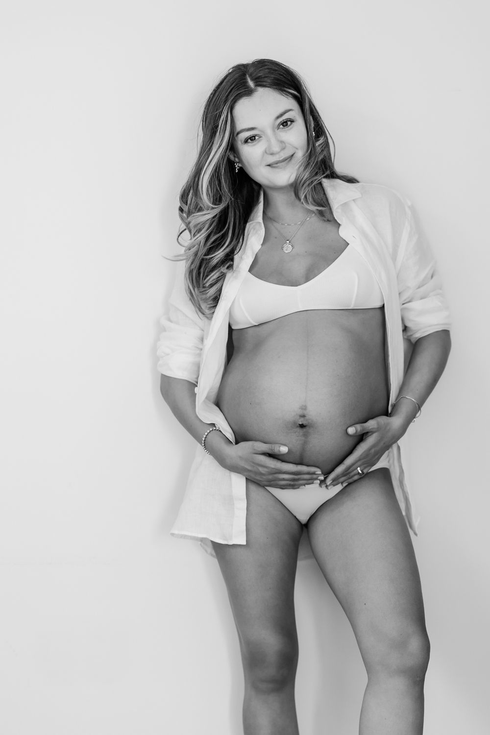 Minimalist pregnancy portrait series with woman in white top showing growing baby bump.