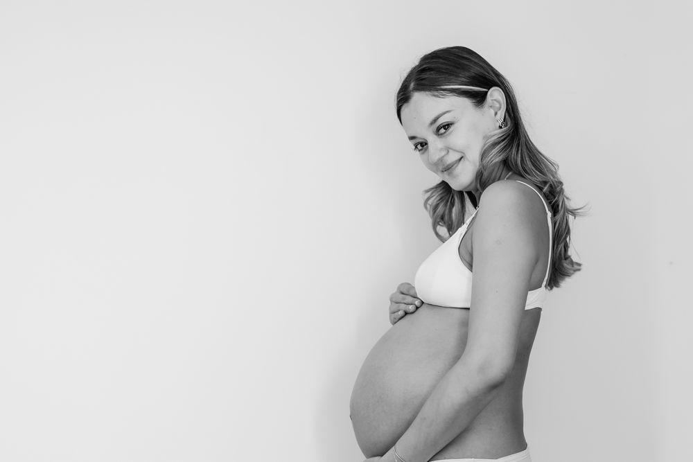 Artistic black and white maternity photo shoot showing an expectant mother in white against a light background.