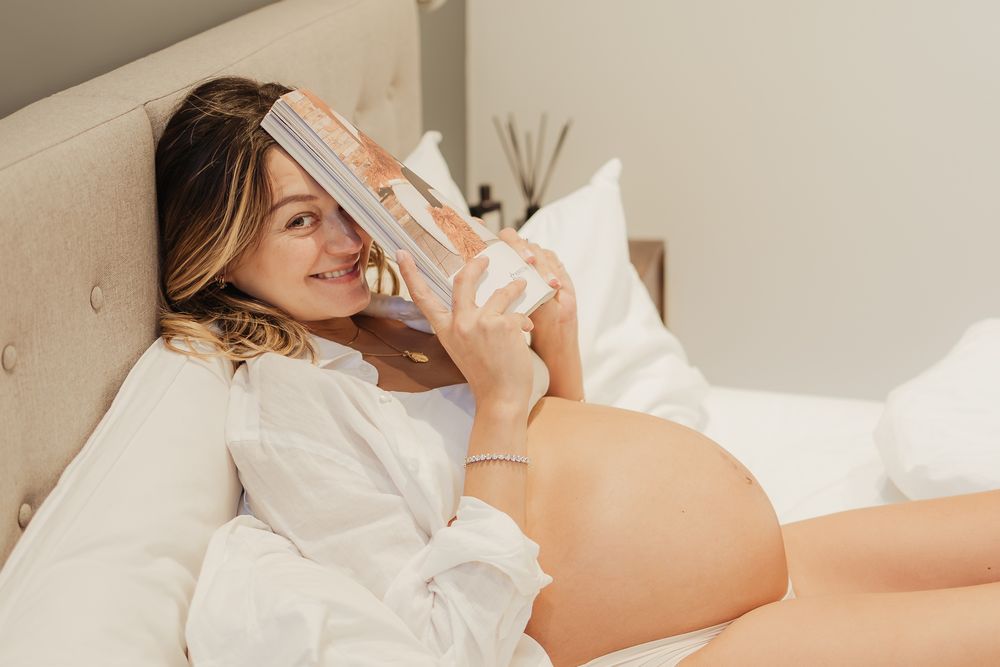 Intimate maternity photos of expecting mother relaxing in bed with natural lighting.