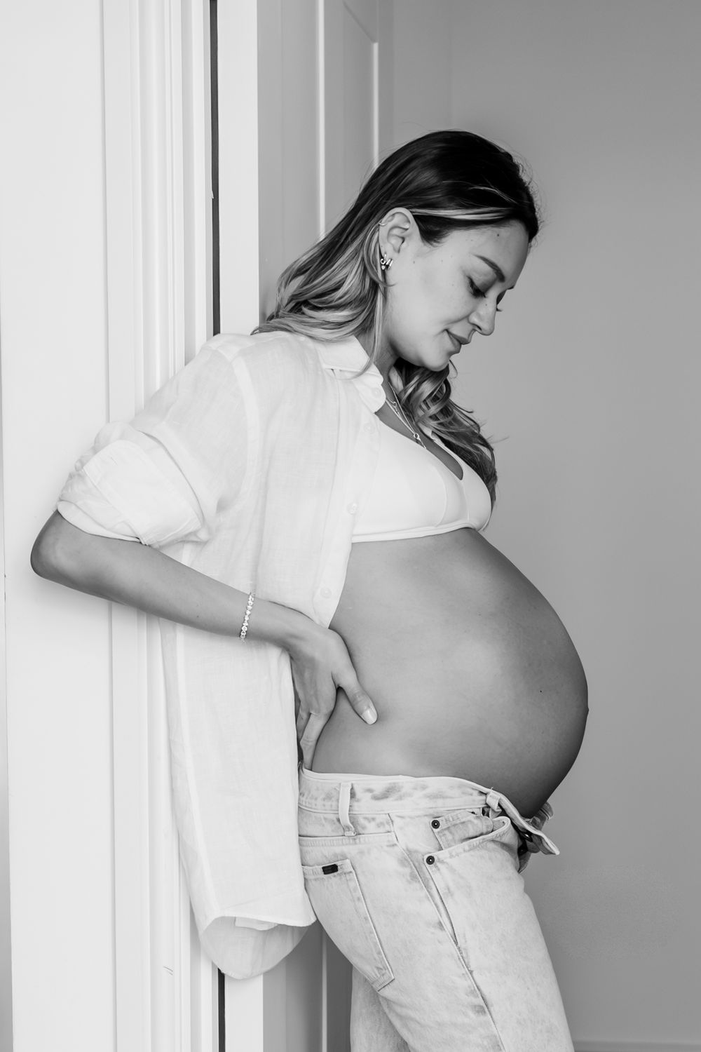 Black and white pregnancy progression photos showing growing belly in casual white attire.