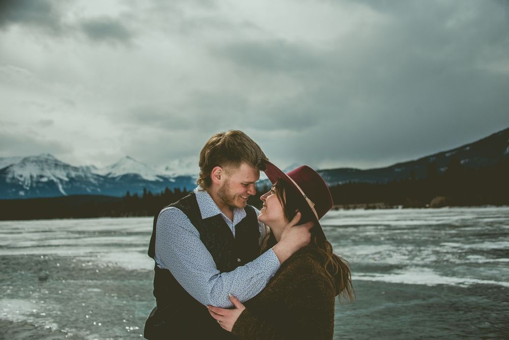 A romantic couple embraces among dramatic mountain scenery and stormy skies in a moody outdoor photoshoot. Jasper Engagement Photographer