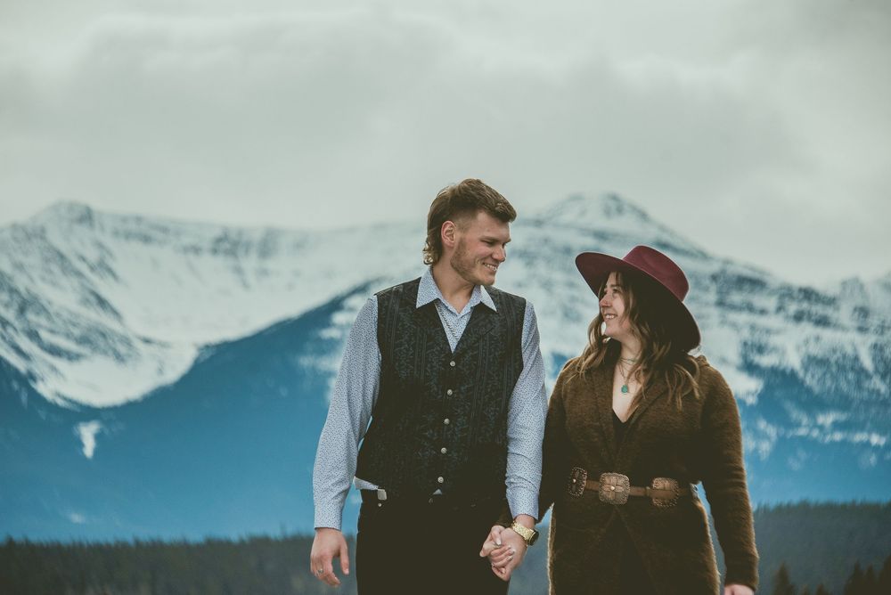 A romantic couple walks hand in hand through a snowy mountain landscape with snow-capped peaks Jasper Engagement Photographer