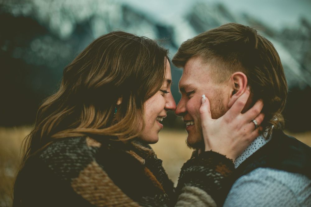 A couple embracing in a snowy winter setting with mountains in the background. Jasper Engagement Photographer