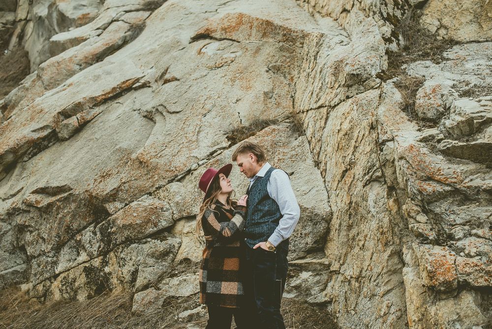 Couple poses intimately against a rocky cliff face with mountains in the background Jasper Engagement Photographer