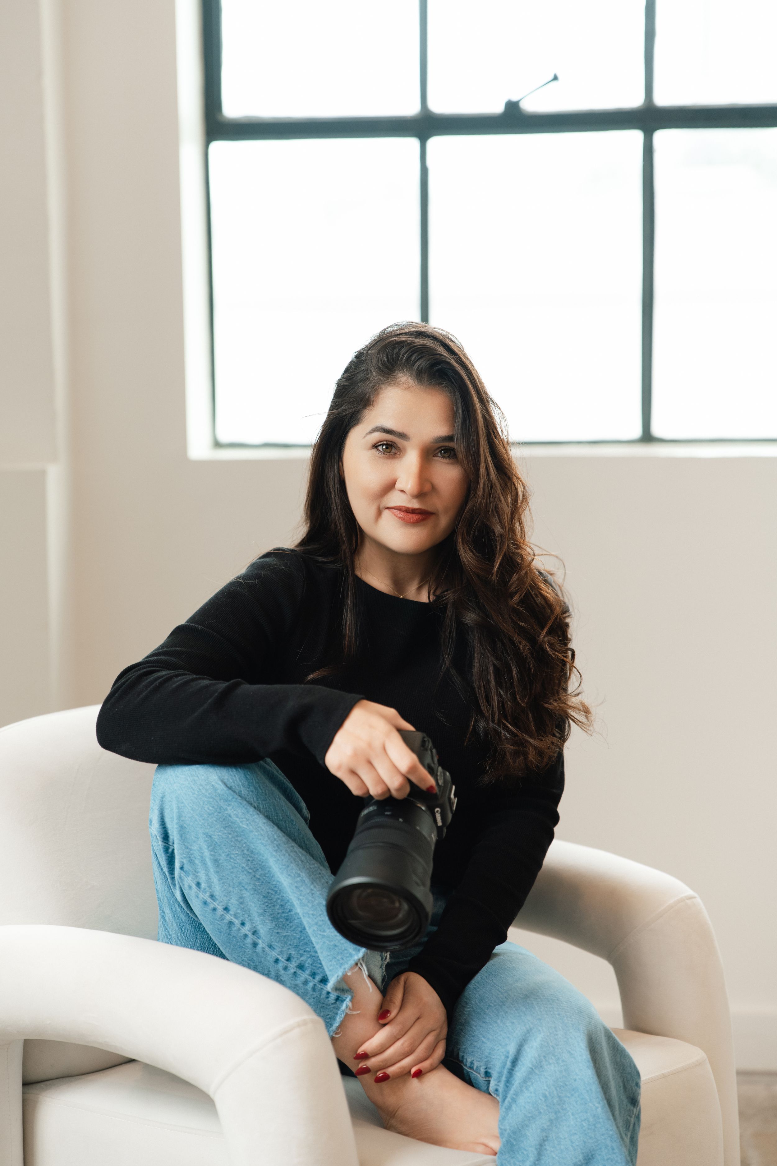 A photographer in casual attire sits on white floor with photography equipment and laptop around them.