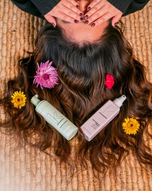 Hair care products displayed with colorful flowers on textured carpet background.