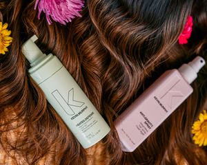 Close up of hair products arranged with pink and yellow flowers on woven surface.