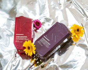 Beauty product flatlay with purple boxes and yellow sunflowers on silver reflective surface.