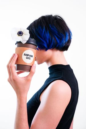 Side profile showing vibrant blue hair and hand holding coffee cup.