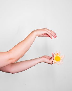 Extended arm holding a vibrant orange flower against white backdrop.
