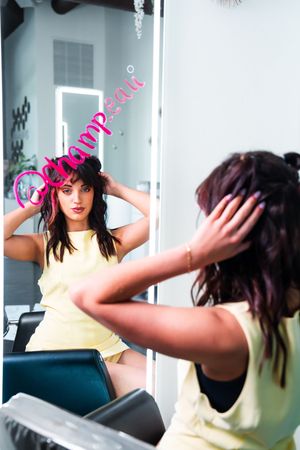 Person in yellow top posing against mirror in studio setting.