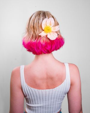 Back view of person wearing white tank top with pink flowers in hair.