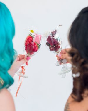 Multiple hands holding up pink cocktails in a celebratory toast.