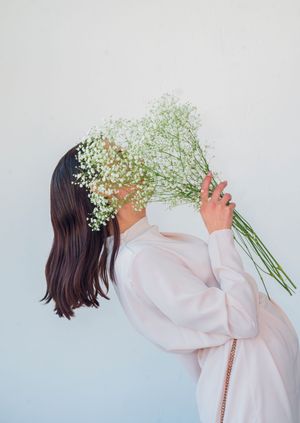 Figure in white holding baby's breath flowers against light background.