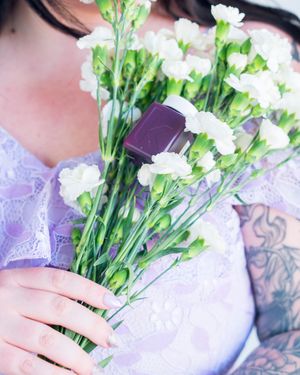 White carnations held against purple fabric with visible tattoo details.