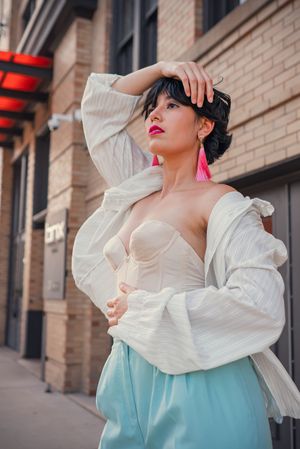 Dramatic fashion poses in white ruffled top and mint skirt against brick wall.